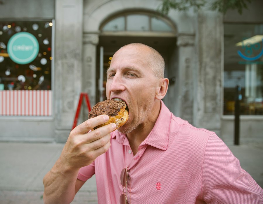 A man taking a big bite of a pastry outside a café