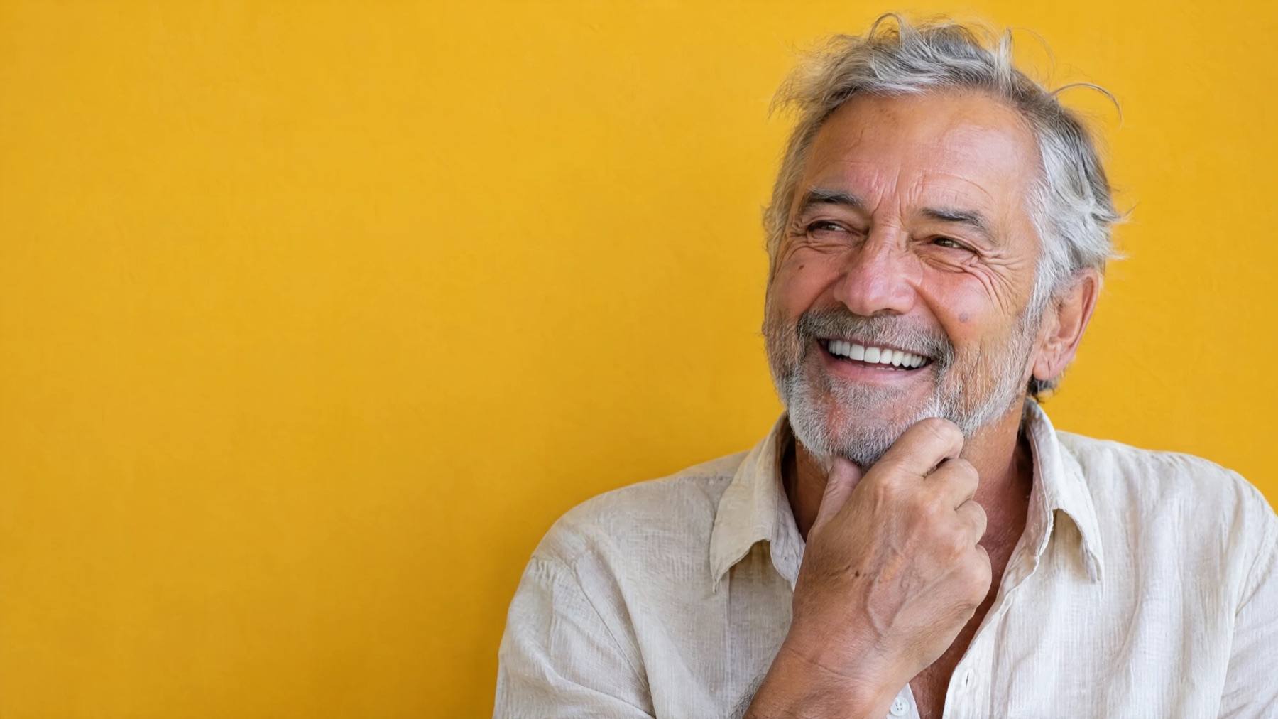 An older man laughing against a yellow wall